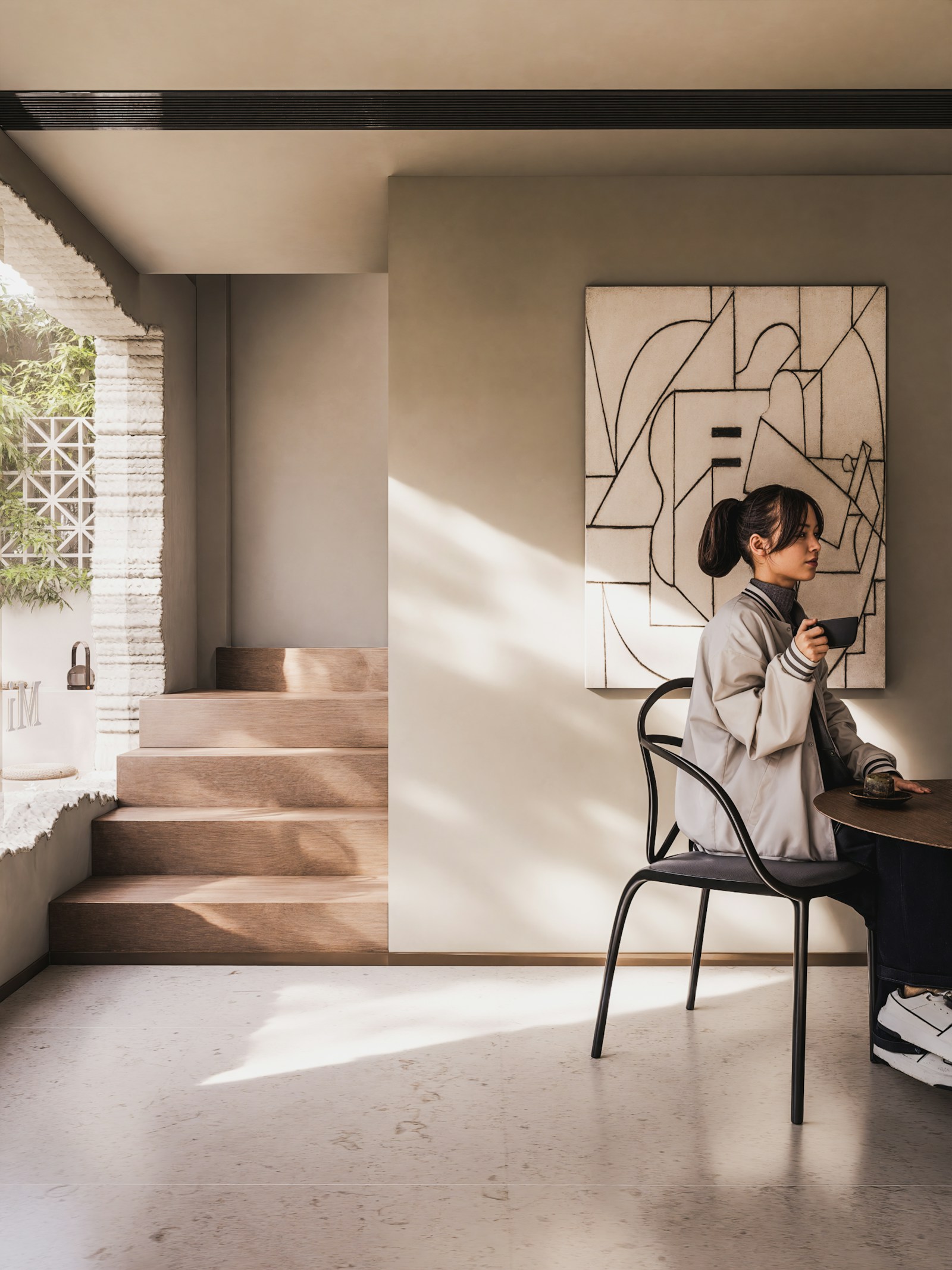 A woman holding a cup of coffee in a soft, sunlit minimal interior